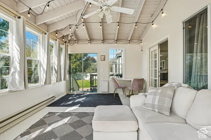 Sunroom with exposed beam ceiling, multiple windows, double sliding glass doors, and a ceiling fan