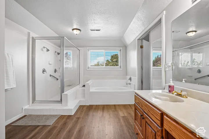 Walk-in shower with clear glass enclosure and multiple shower heads, adjacent soaking tub with tiled surround, wood-finish flooring, and a single vanity with wood cabinetry