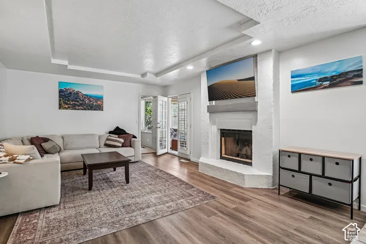 Living area featuring wood-finish flooring, a white brick fireplace, recessed lighting, and a tray ceiling with accent lighting
