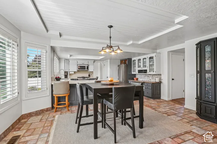 Kitchen with white and gray cabinetry, ceramic tile flooring, kitchen island with seating, a built-in microwave, and plantation shutters