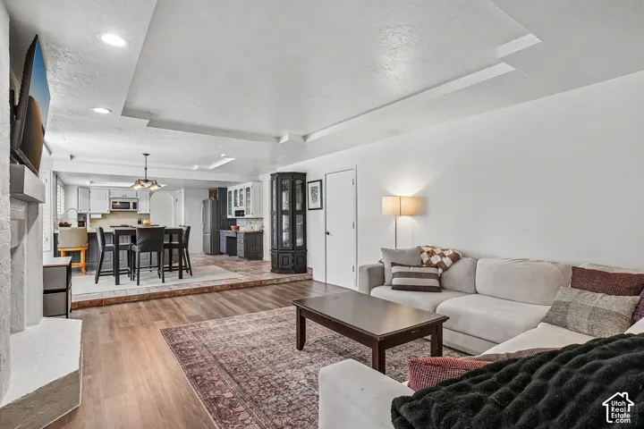 Wood-finish flooring with a raised tile dining area, recessed lighting, and a white fireplace surround