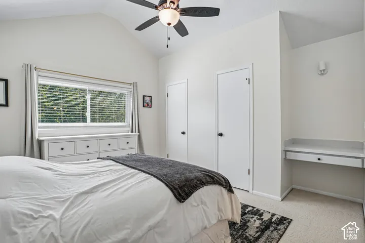Vaulted ceiling with a ceiling fan, dual white closet doors, built-in desk with a single drawer, and a window with blinds
