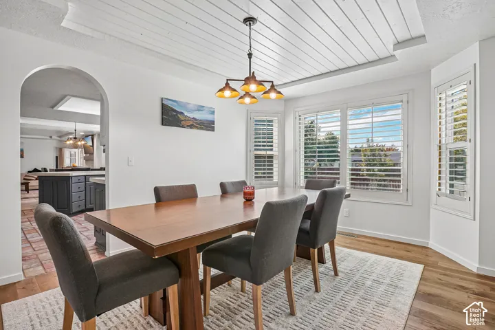 Dining area featuring a shiplap ceiling, a multi-light chandelier, a bay window with plantation shutters, wood-finish flooring, and an arched entryway