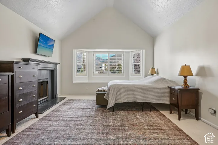 Vaulted ceiling with a bay window featuring white plantation shutters, and a fireplace with a dark mantel