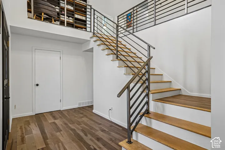 Wood-finish flooring, staircase with metal railing, white walls, and an elevated loft area with built-in shelving