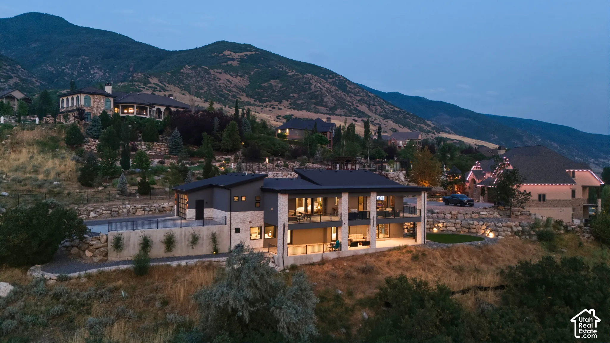 Modern architectural exterior featuring stone and dark siding, extensive glass paneling, multi-level balconies, and a flat roofline