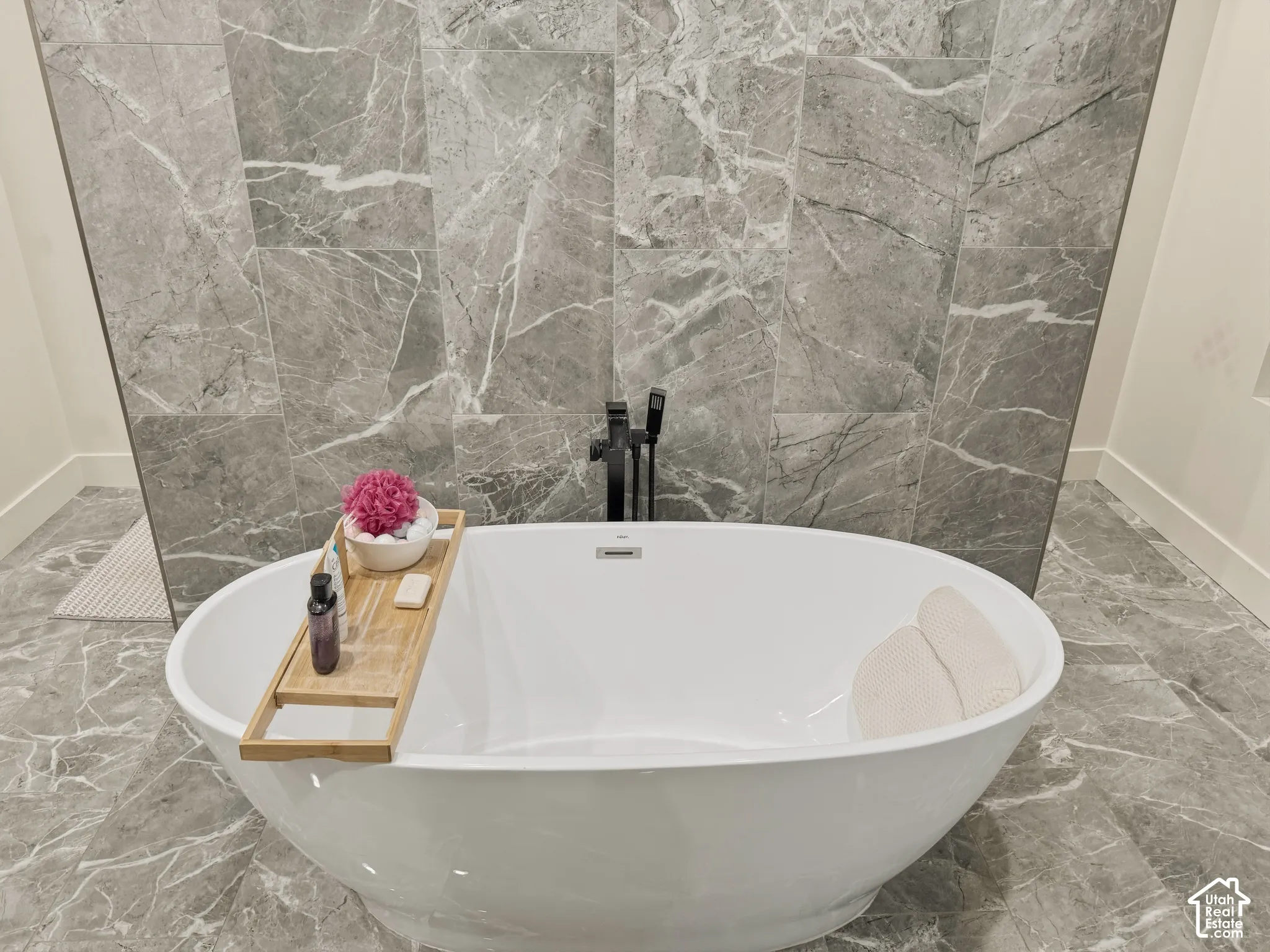 Freestanding soaking tub with a floor-mounted matte black tub filler, complemented by large format gray stone-finish wall and floor tiles