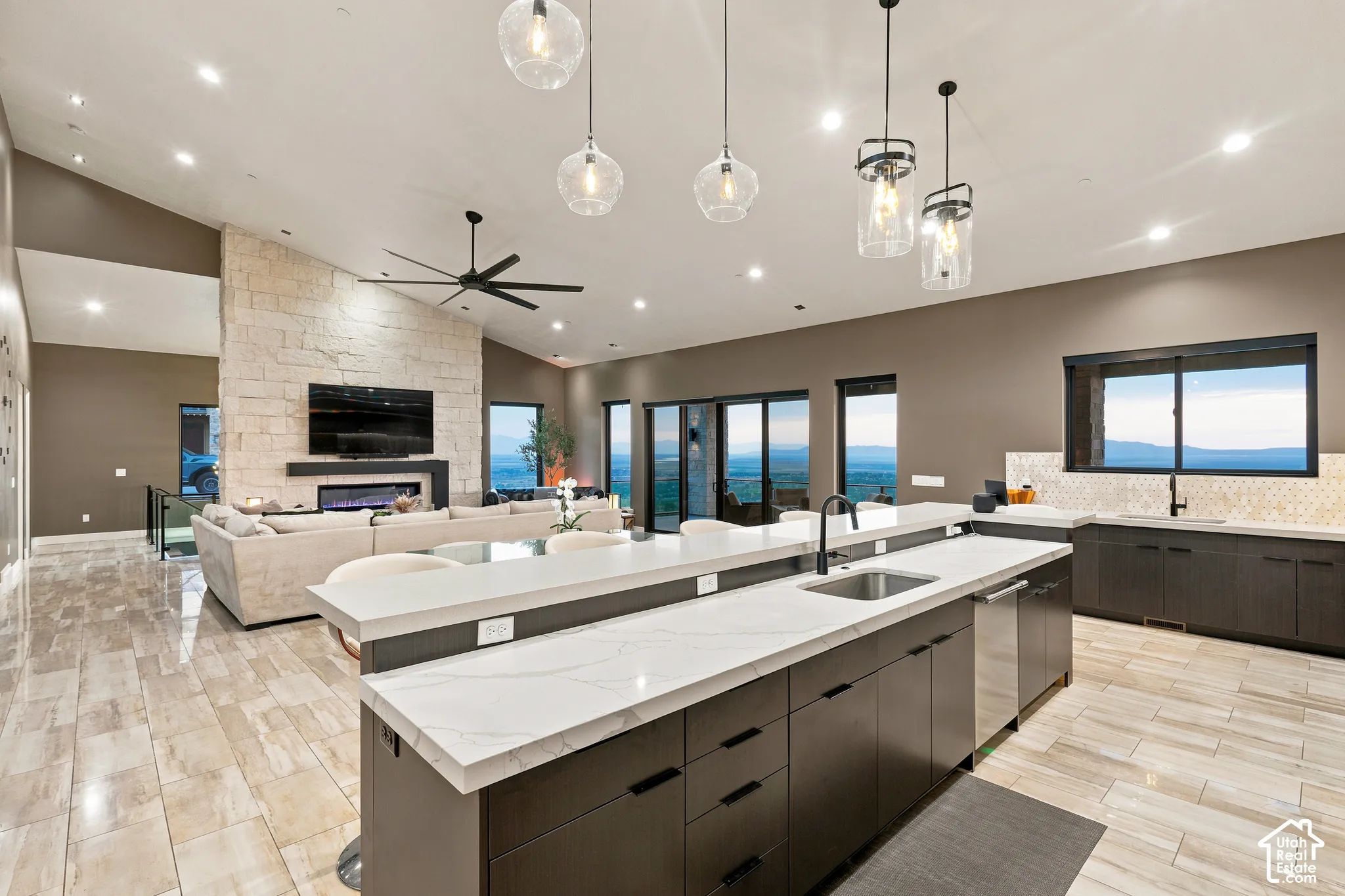 Open-concept living space featuring vaulted ceilings, a stone-clad fireplace, and expansive windows