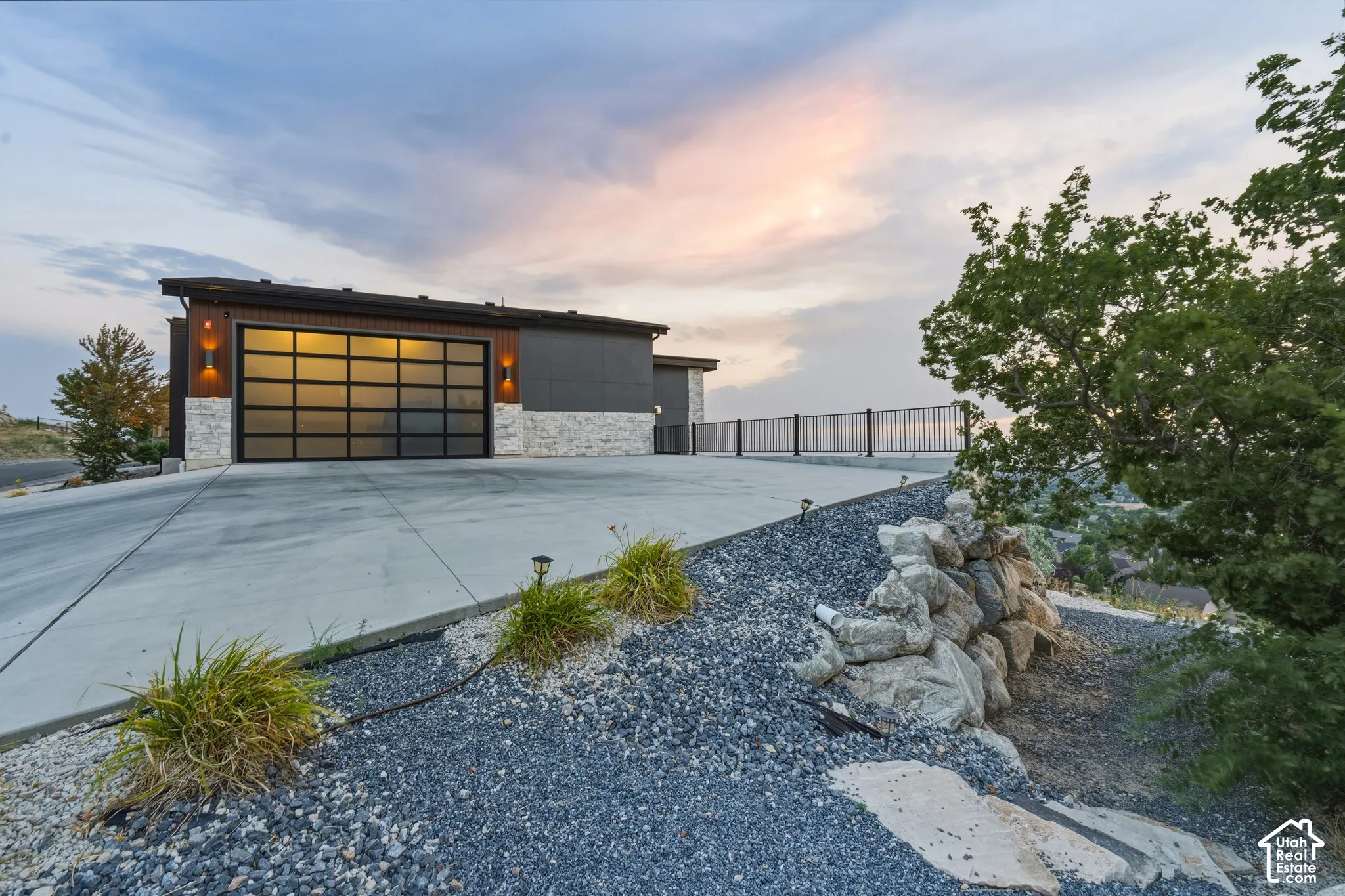 Modern garage door with frosted glass panels, stone accents, exterior lighting fixtures, and a concrete driveway