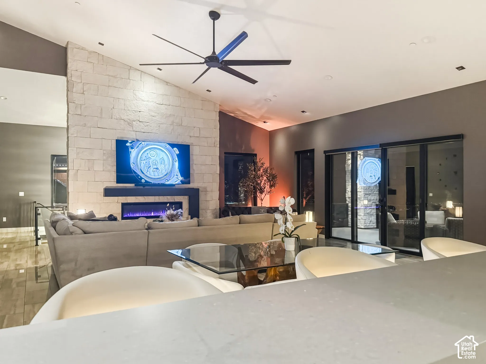 Vaulted ceiling with an exposed beam and ceiling fan, stone-clad fireplace with an electric insert, recessed lighting, and large sliding glass doors