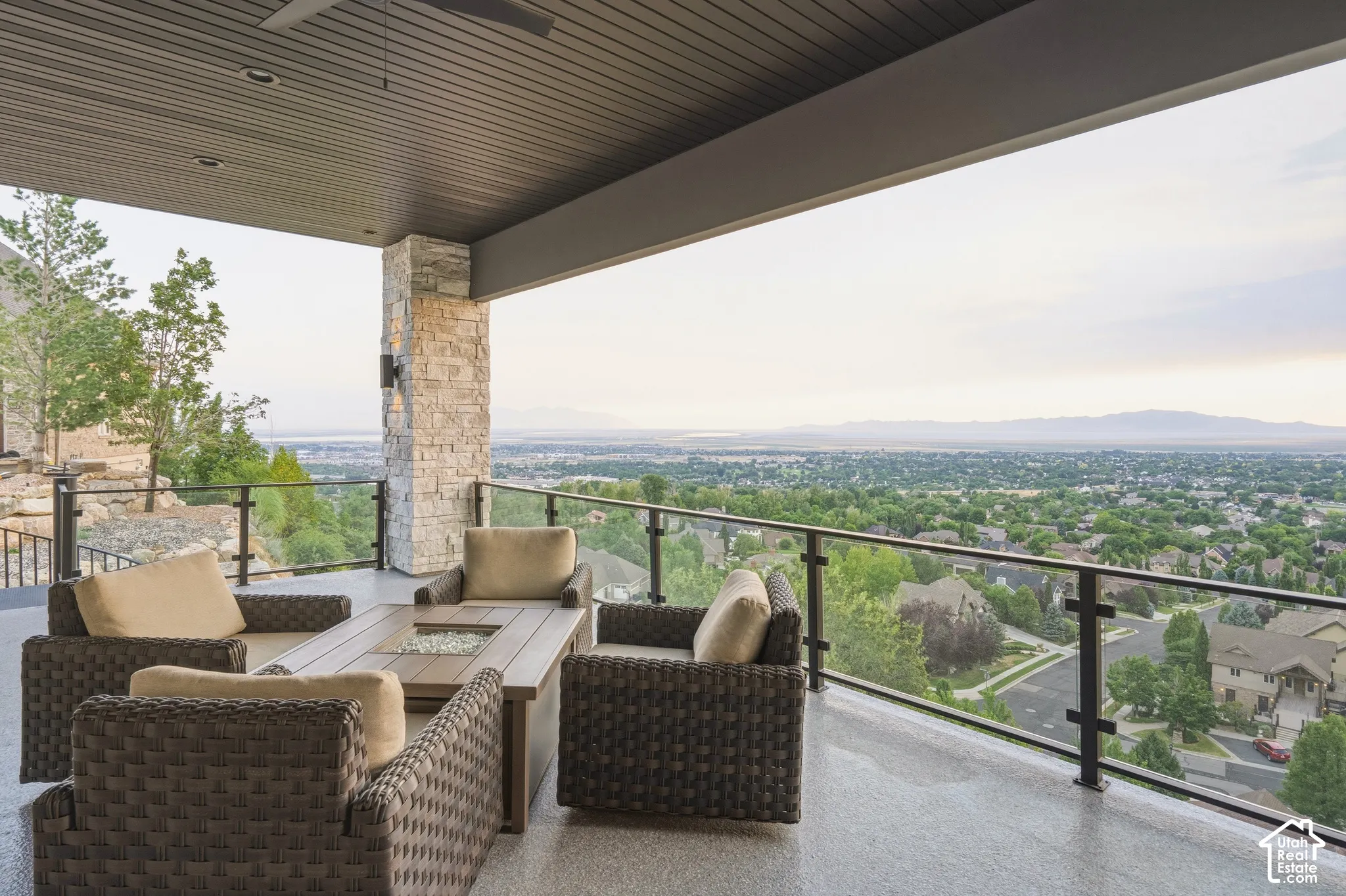 Expansive covered patio featuring a stone-clad pillar, glass panel railing, and a dark wood-finish ceiling