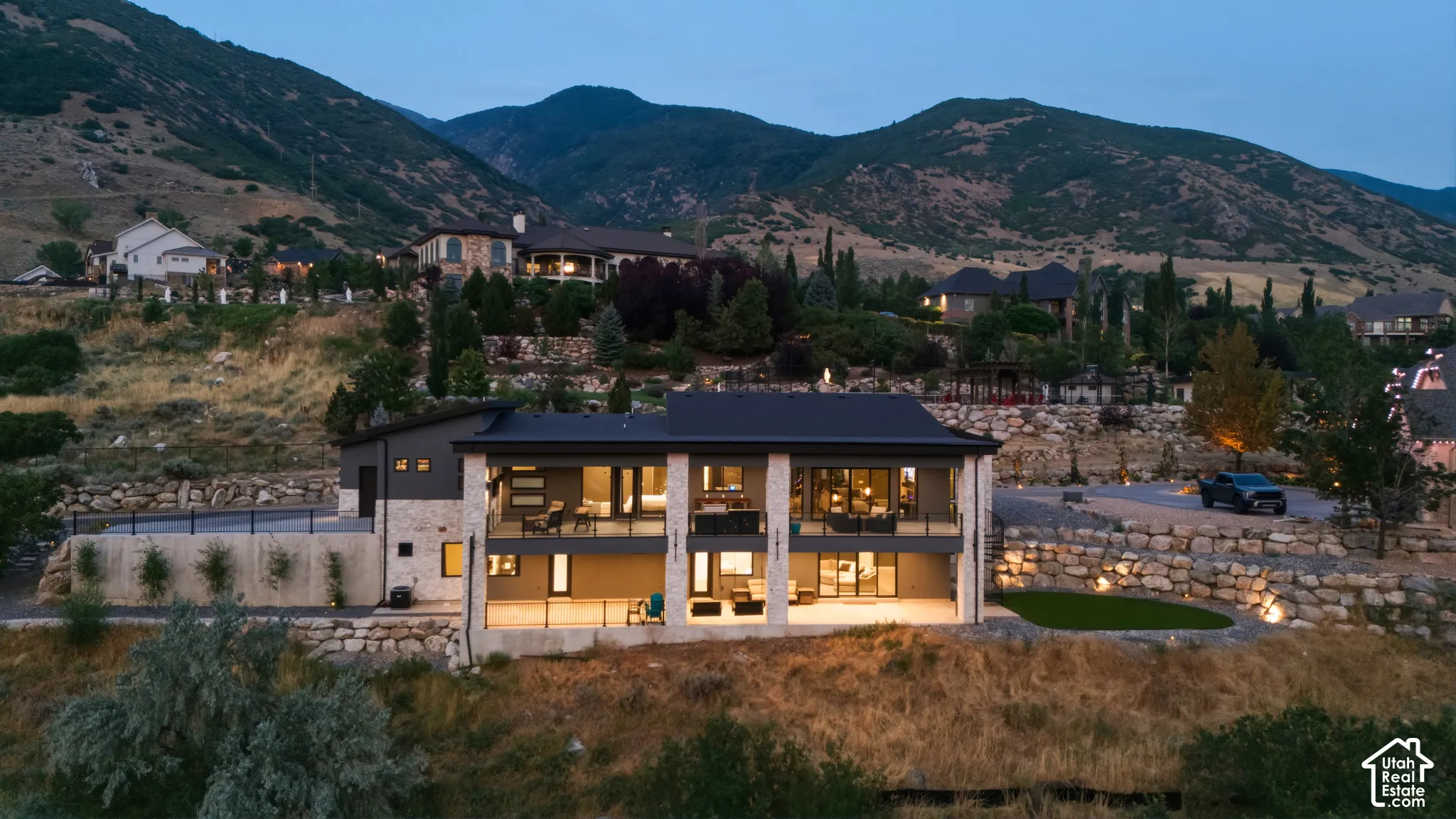 Modern architecture with expansive windows, multiple balconies, stone facade accents, a sloped roofline, and integrated outdoor lighting