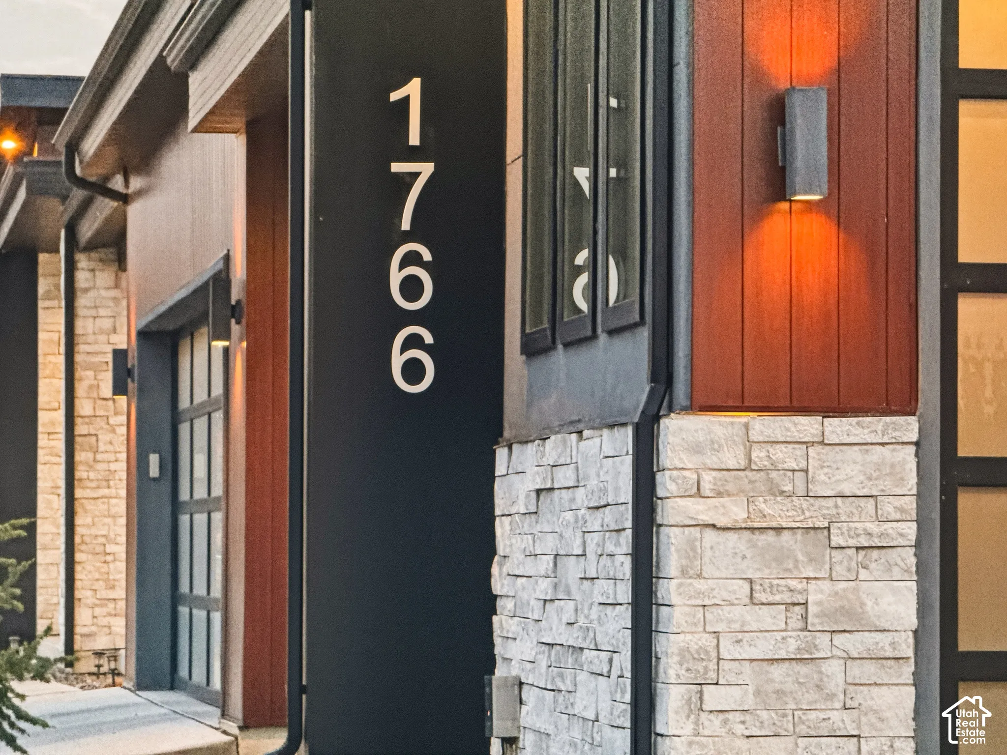 Architectural exterior featuring a blend of vertical wood-finish siding, stone accents, modern wall sconces, and large exterior house numbers