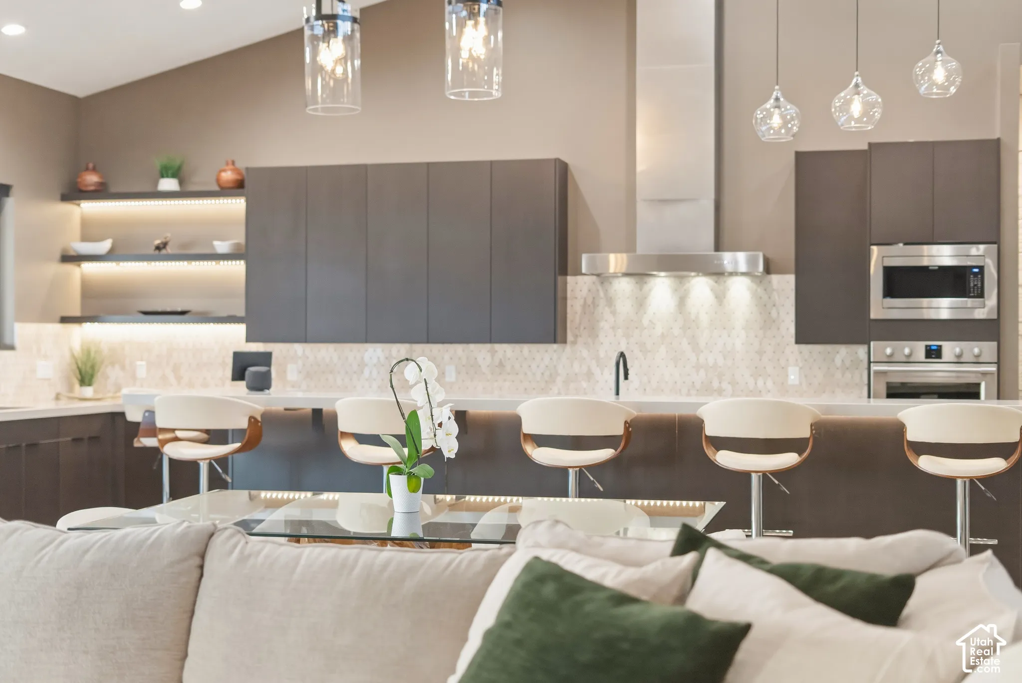 Kitchen featuring dark flat-panel cabinetry, light-toned countertops, a mosaic tile backsplash, and stainless steel appliances