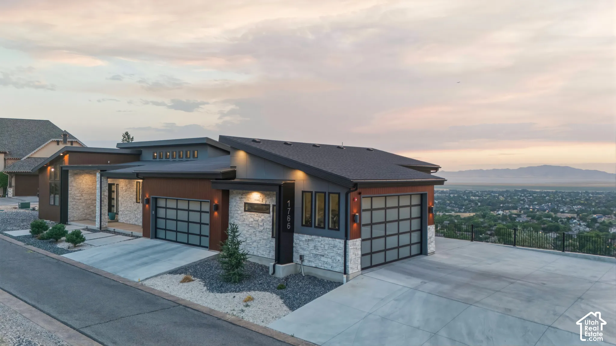Modern architectural exterior with a low-slope roof design, stone veneer accents, two-car garage with frosted glass panels, and concrete driveway