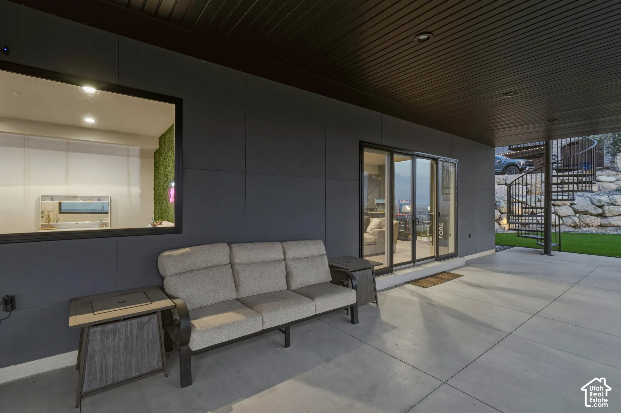 Covered patio with concrete surface, dark paneling, and a black spiral staircase