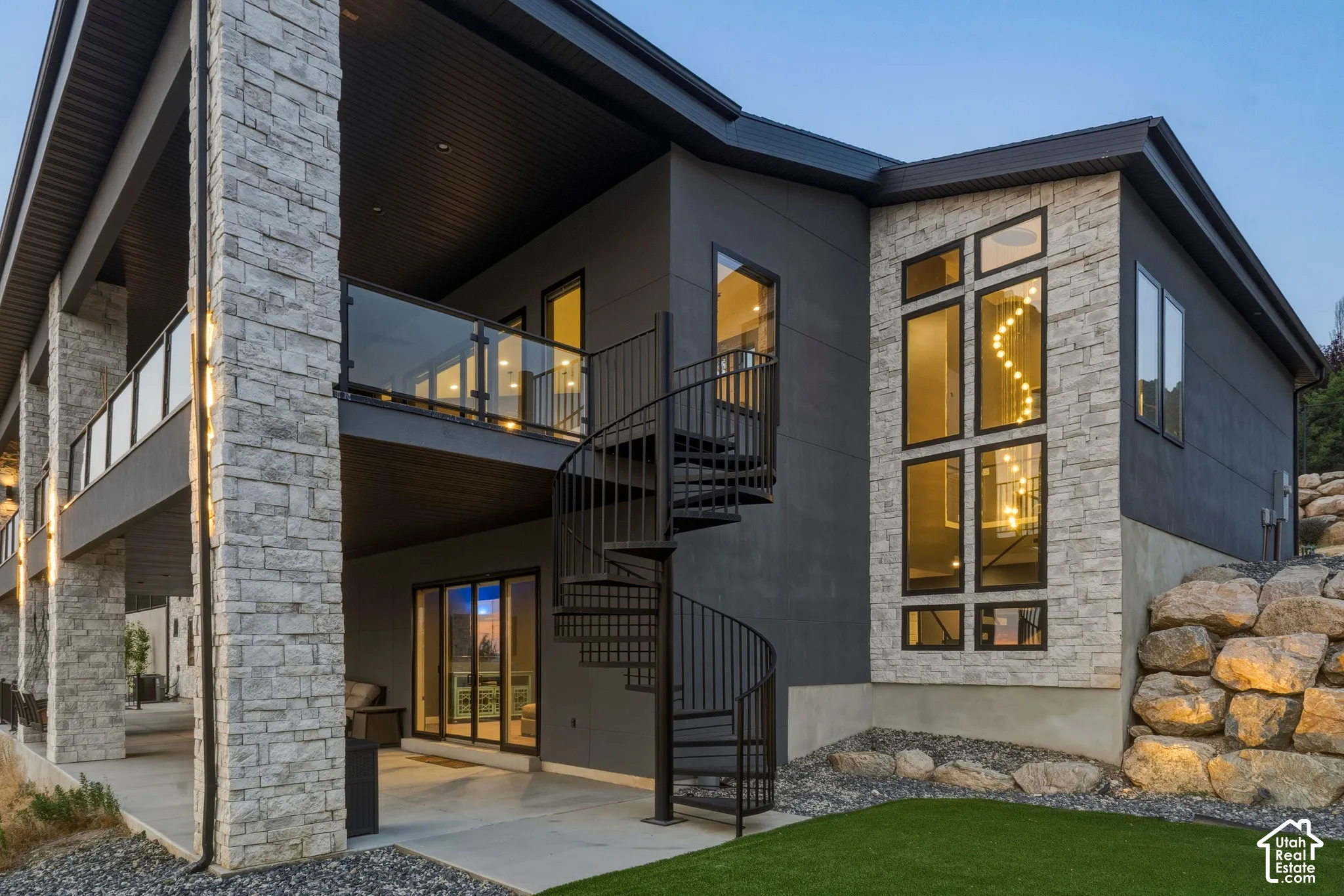Multi-level exterior featuring stone cladding, a spiral staircase, glass panel railings, and expansive windows