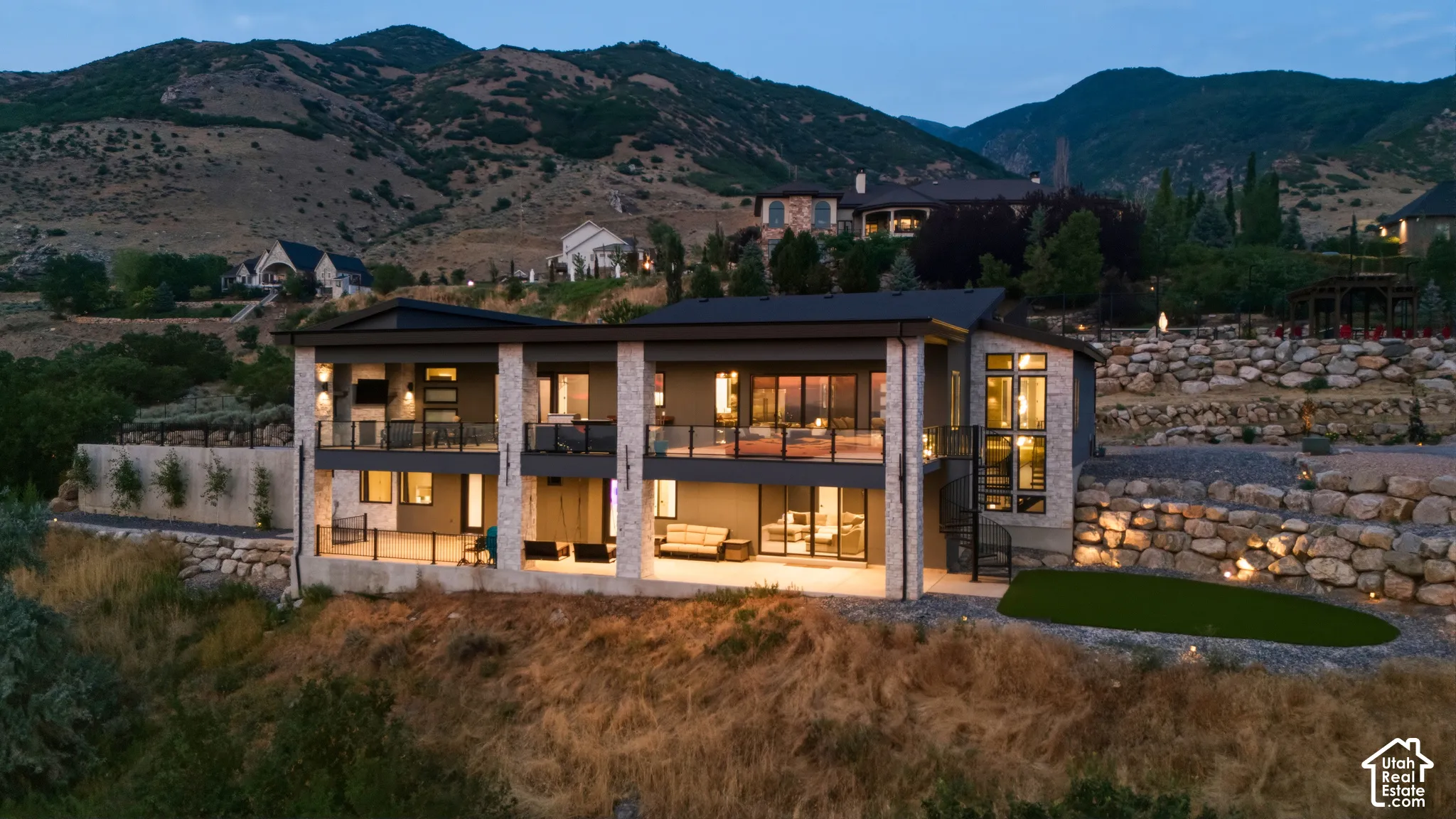 Contemporary residence featuring multiple balconies, stone facade accents, expansive window placements, and a tiered rock wall landscape