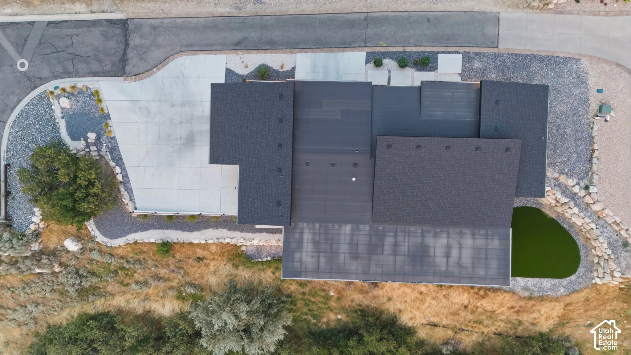 Modern architectural design with a multi-level roofline, extensive paved driveway, and gravel landscaping