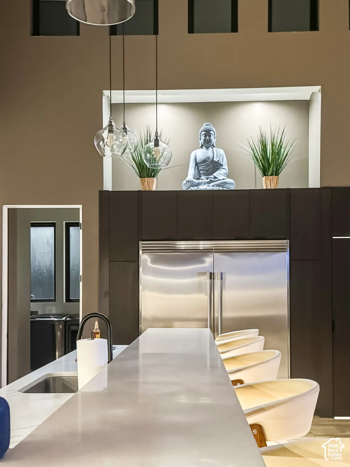 Integrated stainless steel refrigerator, recessed lighting, sleek dark cabinetry, and pendant lighting