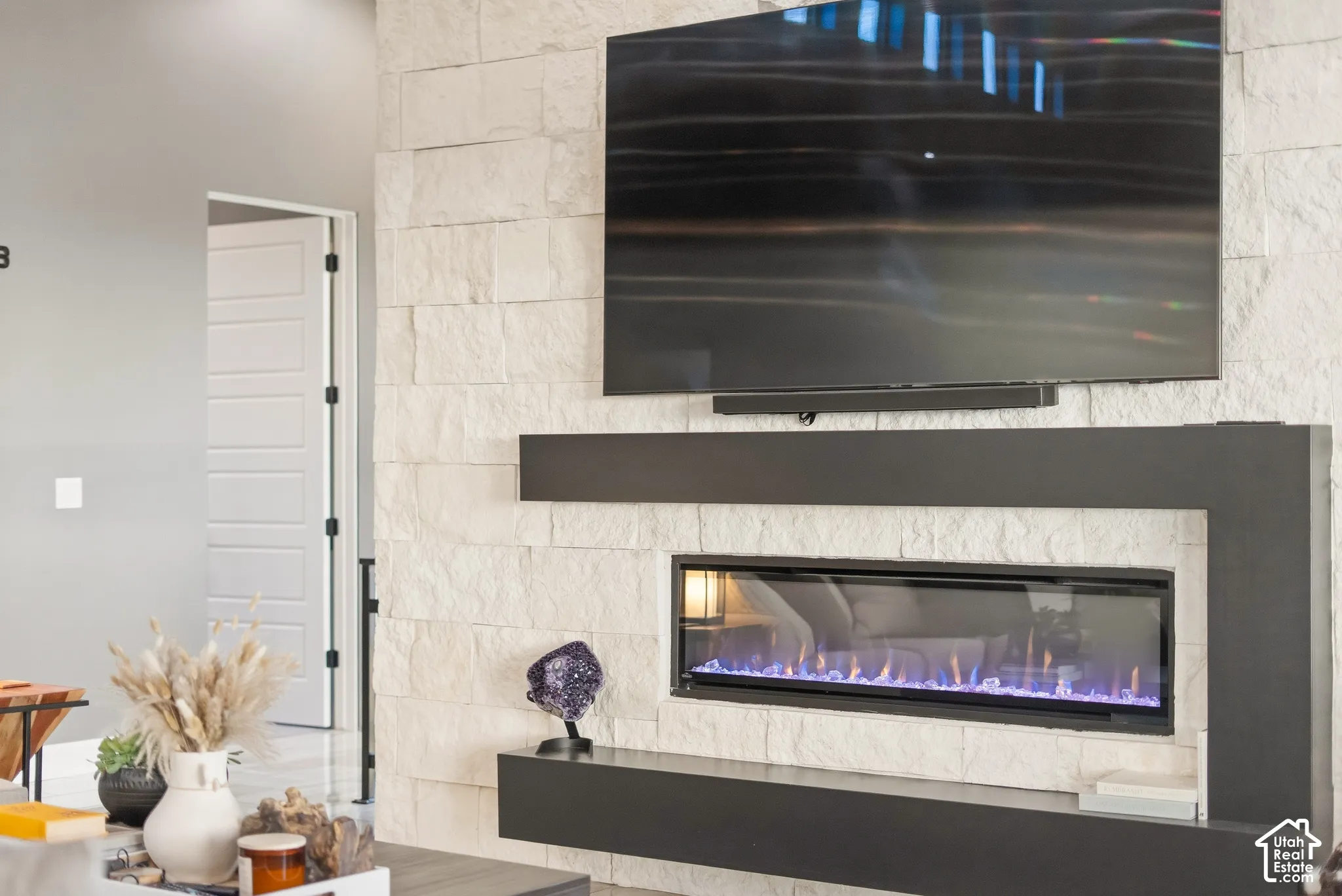 Stacked stone fireplace with an integrated electric insert, mounted television, and floating shelving