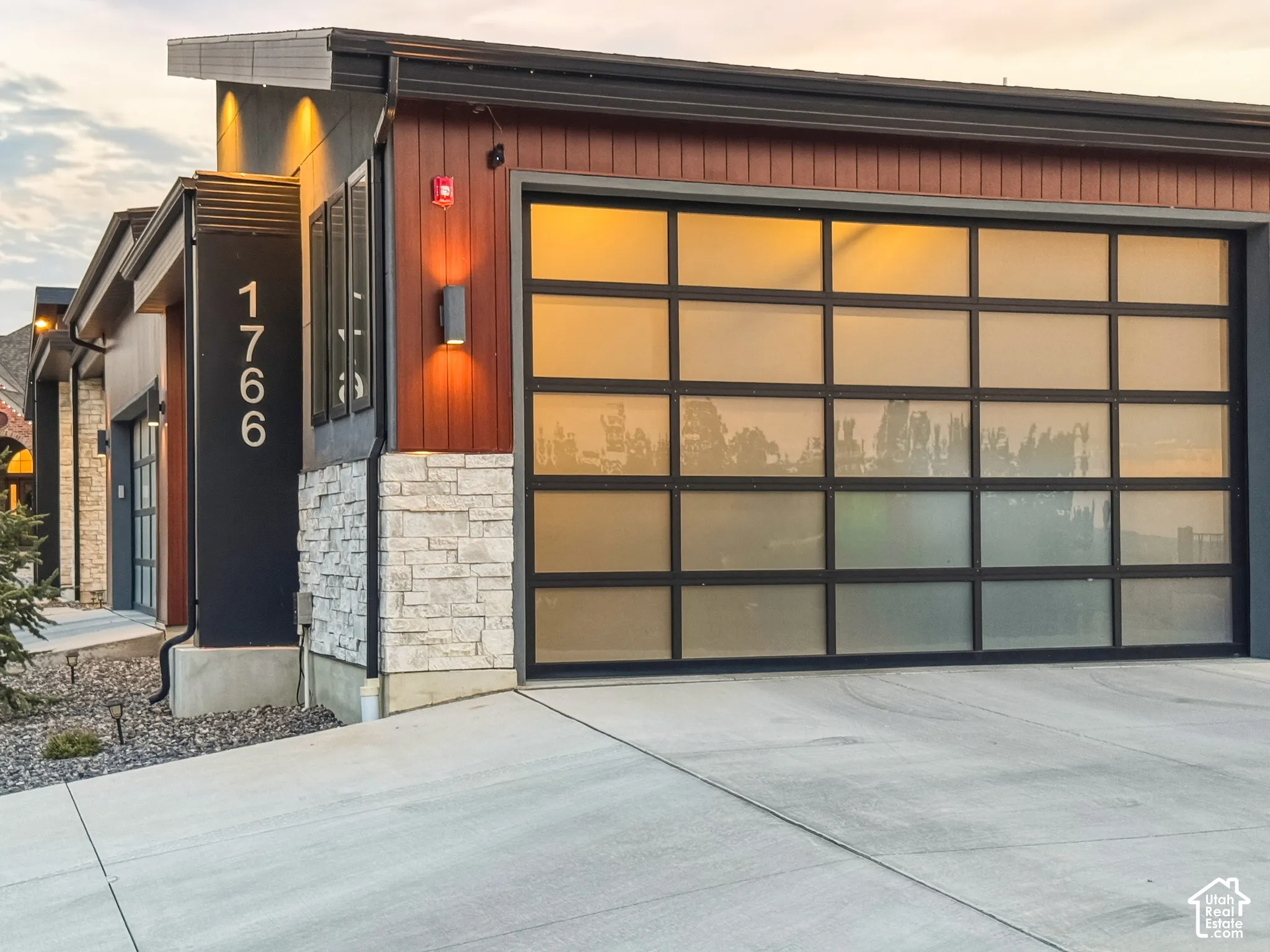 Modern exterior featuring a prominent frosted glass garage door, stone accent siding, and contemporary lighting fixtures