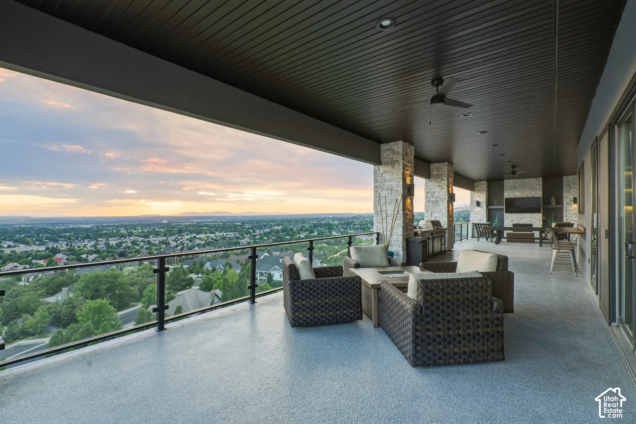 Expansive covered patio with a textured floor, stone accent columns, and a glass railing system