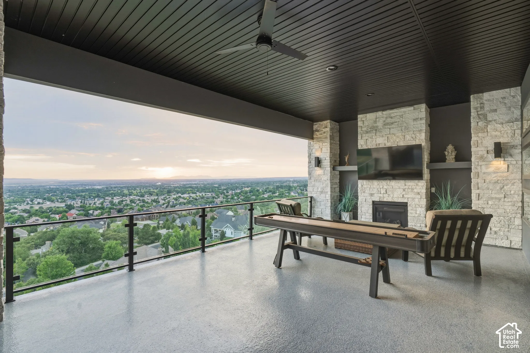 Covered patio with a stone-clad fireplace and media built-in, featuring a glass and metal railing, ceiling fan, and recessed lighting