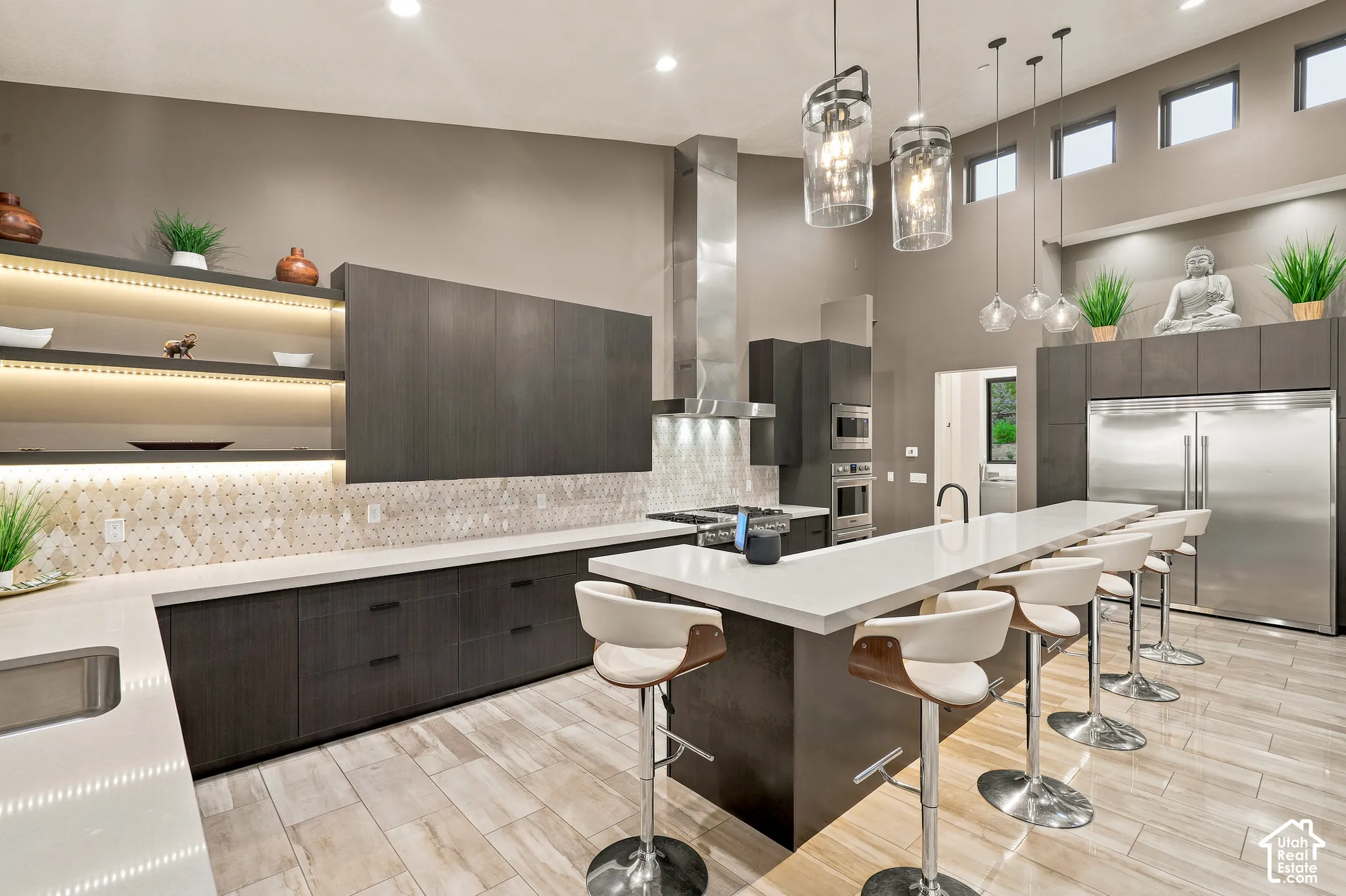 Modern kitchen featuring a large island with seating, stainless steel appliances, and integrated shelving with accent lighting