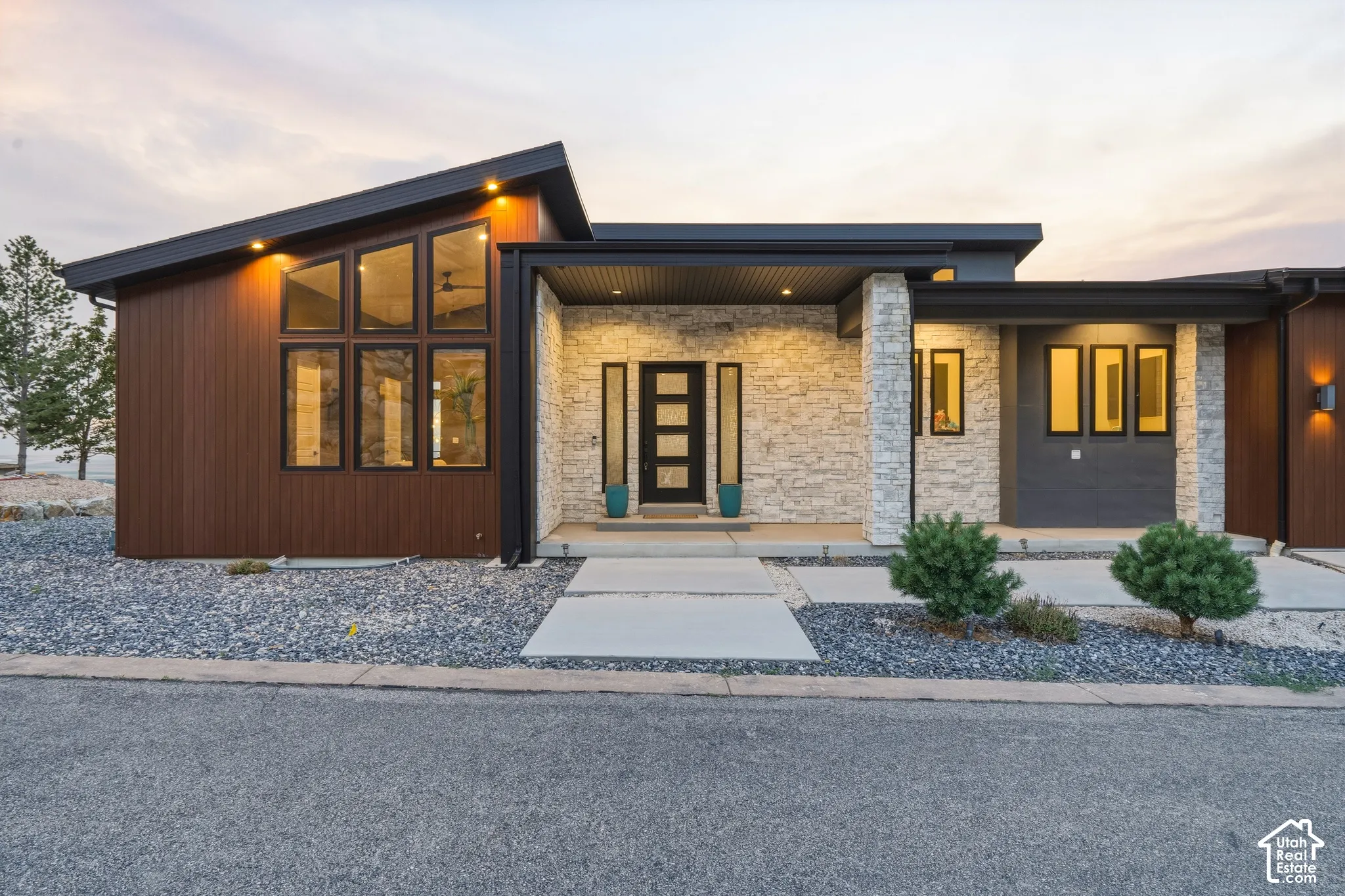Modern exterior with a sloped roofline, stacked stone accents, wood-finish siding, and large angular windows