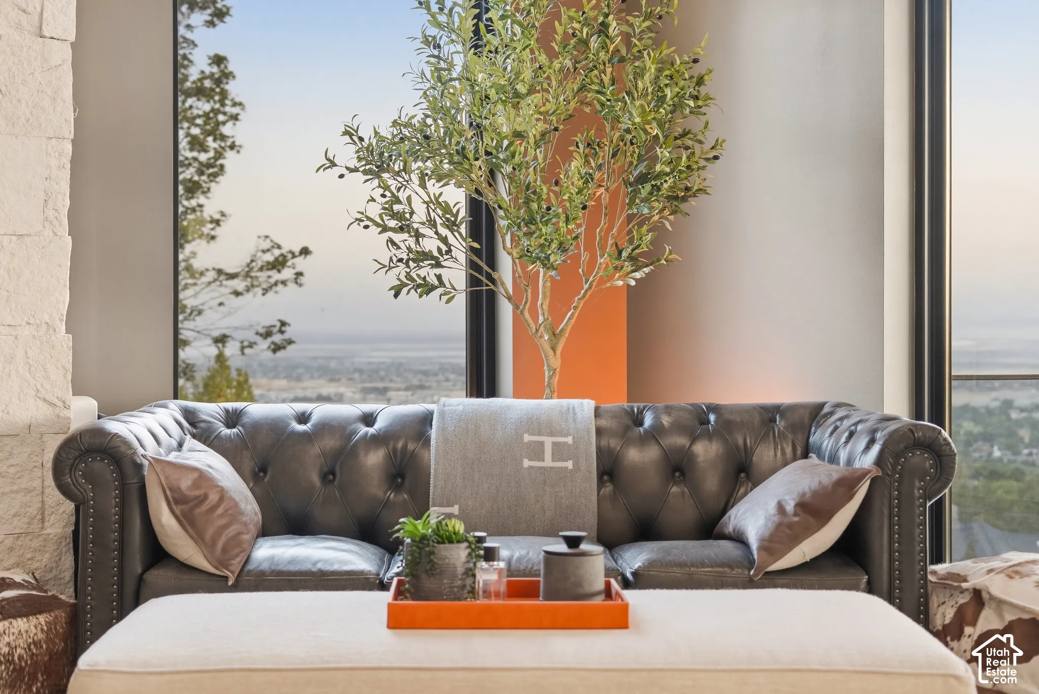 Expansive windows offering broad outdoor scenery, stone accent wall, and a refined seating area with a tufted sofa