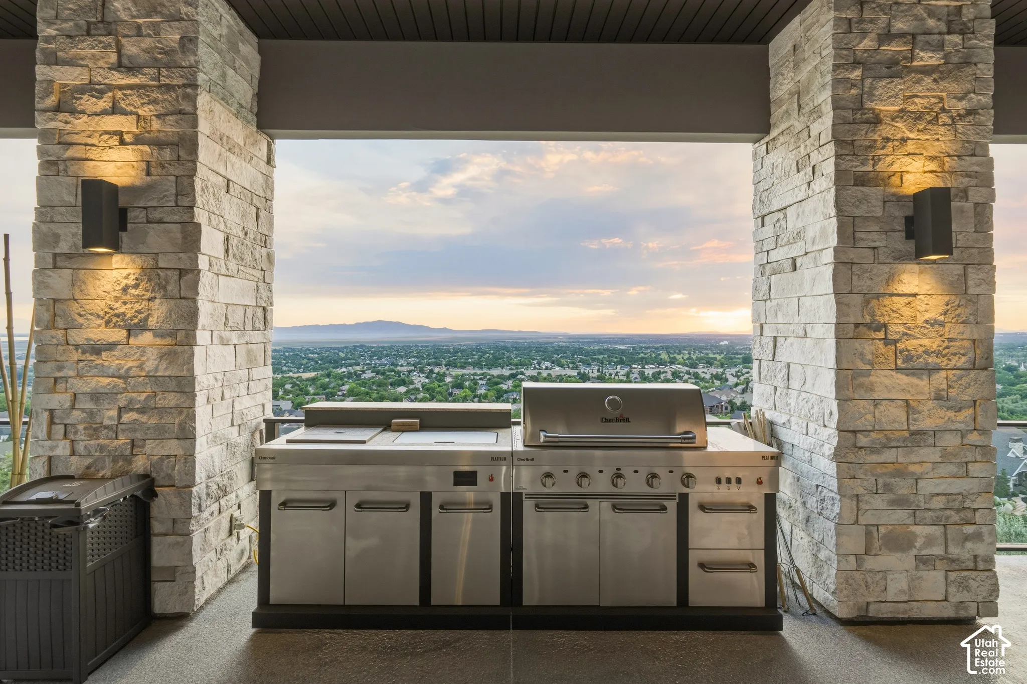 Outdoor kitchen featuring stainless steel appliances, stone columns, integrated lighting, and a textured ceiling