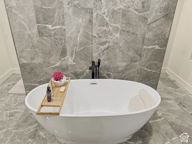 Freestanding soaking tub with a floor-mounted matte black tub filler, complemented by large format gray stone-finish wall and floor tiles