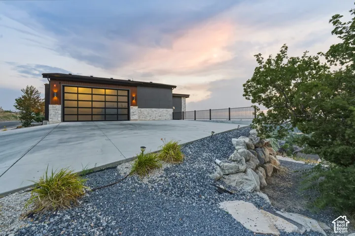 Modern garage door with frosted glass panels, stone accents, exterior lighting fixtures, and a concrete driveway