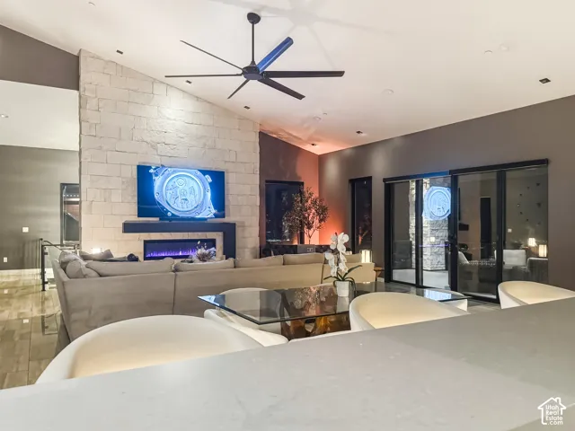 Vaulted ceiling with an exposed beam and ceiling fan, stone-clad fireplace with an electric insert, recessed lighting, and large sliding glass doors