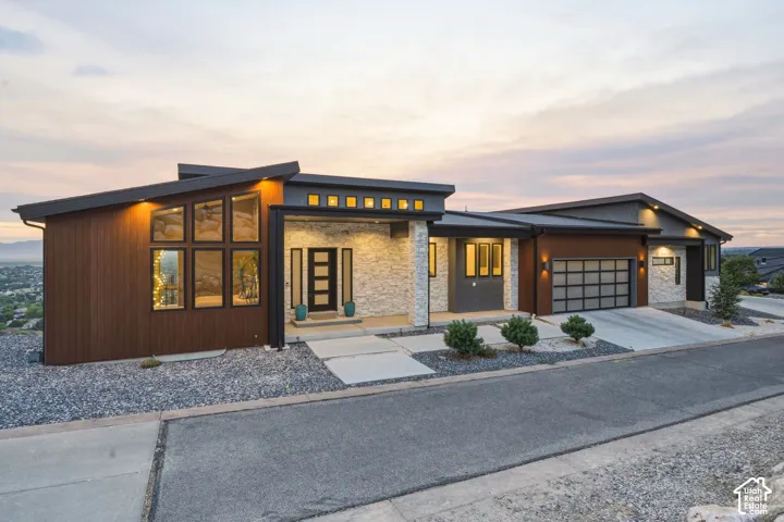 Modern architectural exterior featuring a sloped roofline, stacked stone accents, wood-finish siding, a frosted glass garage door, and a multi-pane entry door