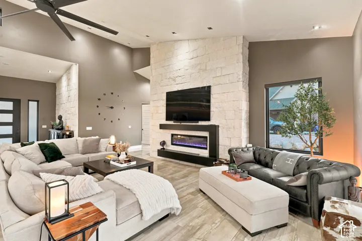 Vaulted ceilings, a stone-clad fireplace with an electric insert, wood-finish flooring, and a modern ceiling fan