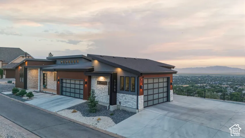 Modern architectural exterior with a low-slope roof design, stone veneer accents, two-car garage with frosted glass panels, and concrete driveway