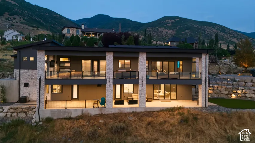 Contemporary exterior with stone pillar accents, multiple covered balconies with glass railings, an expansive lower-level patio, and surrounding mountainous terrain