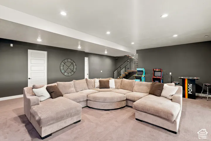 Recessed lighting illuminates a spacious room featuring a modern staircase with a black handrail, dark gray walls, and light-colored carpeting