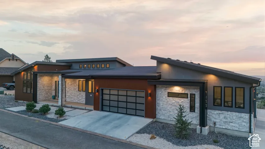 Modern architectural design with a sloped roofline, stone veneer accents, integrated garage with frosted glass panels, and multiple exterior lighting fixtures