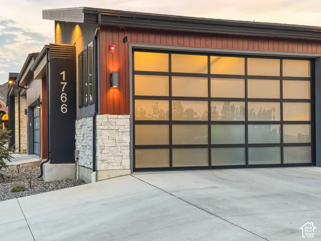 Modern exterior featuring a prominent frosted glass garage door, stone accent siding, and contemporary lighting fixtures