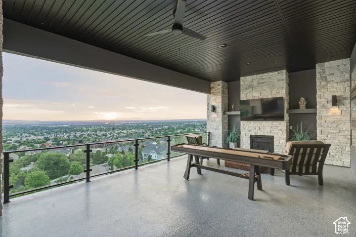 Covered patio with a stone-clad fireplace and media built-in, featuring a glass and metal railing, ceiling fan, and recessed lighting