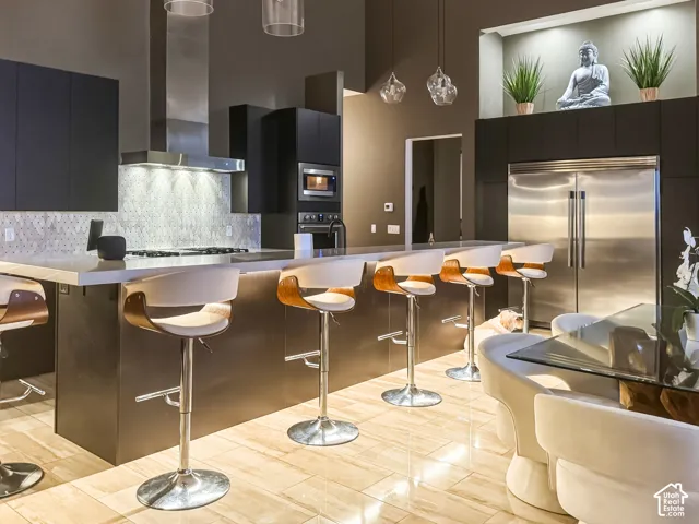 Gourmet kitchen with stainless steel appliances, dark flat-panel cabinetry, light-toned tile flooring, and a large central island