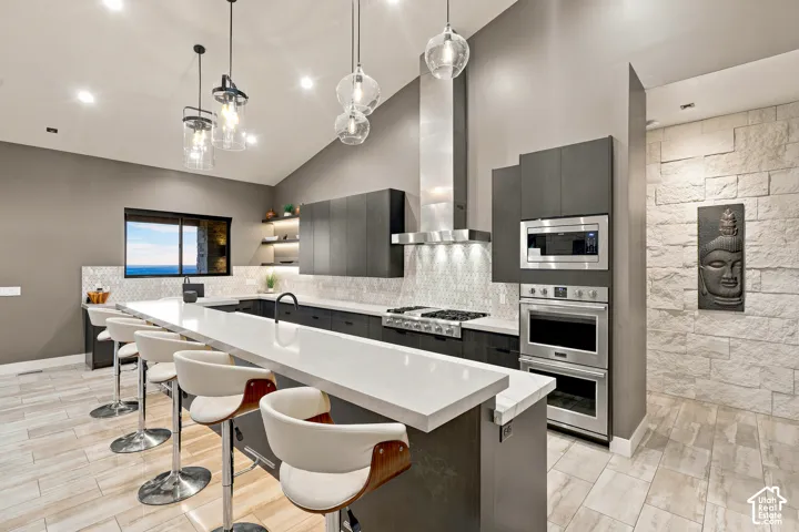 Modern kitchen featuring a large island with white countertop, dark wood-finish cabinetry, stainless steel appliances, and a stacked stone accent wall