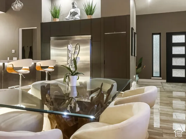 Stainless steel refrigerator, built-in cabinetry, glass-top dining table, wood-finish flooring, and a modern entry door with decorative glass inserts