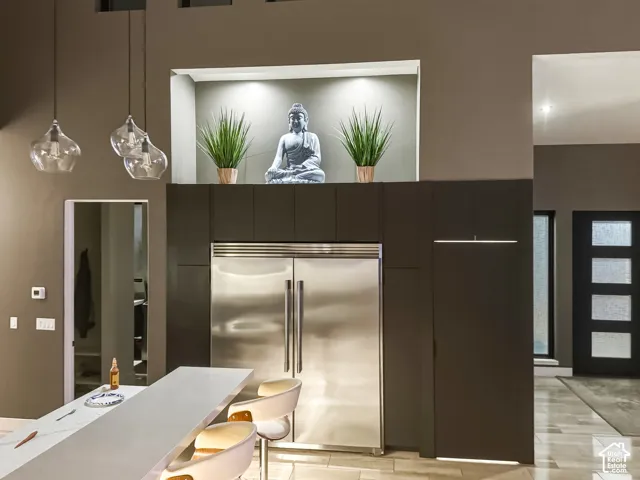 Full-size integrated refrigerator, dark flat-panel cabinetry, three pendant light fixtures, built-in display niche with accent lighting, and a white countertop island