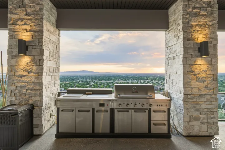 Outdoor kitchen featuring stainless steel appliances, stone columns, integrated lighting, and a textured ceiling