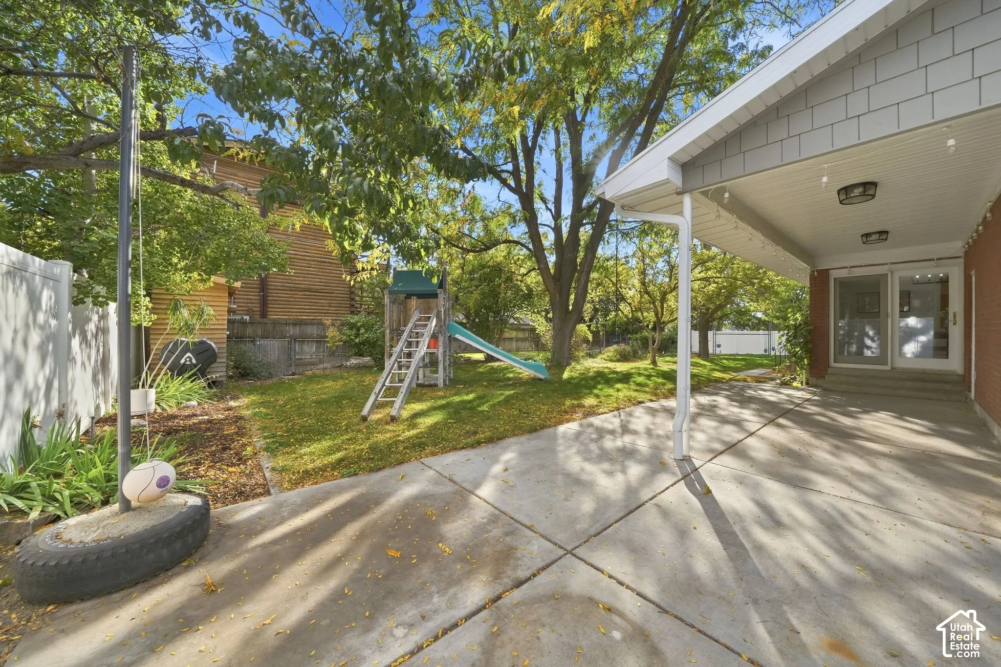 Covered patio overlooking the lawn, play area, and mature trees.
