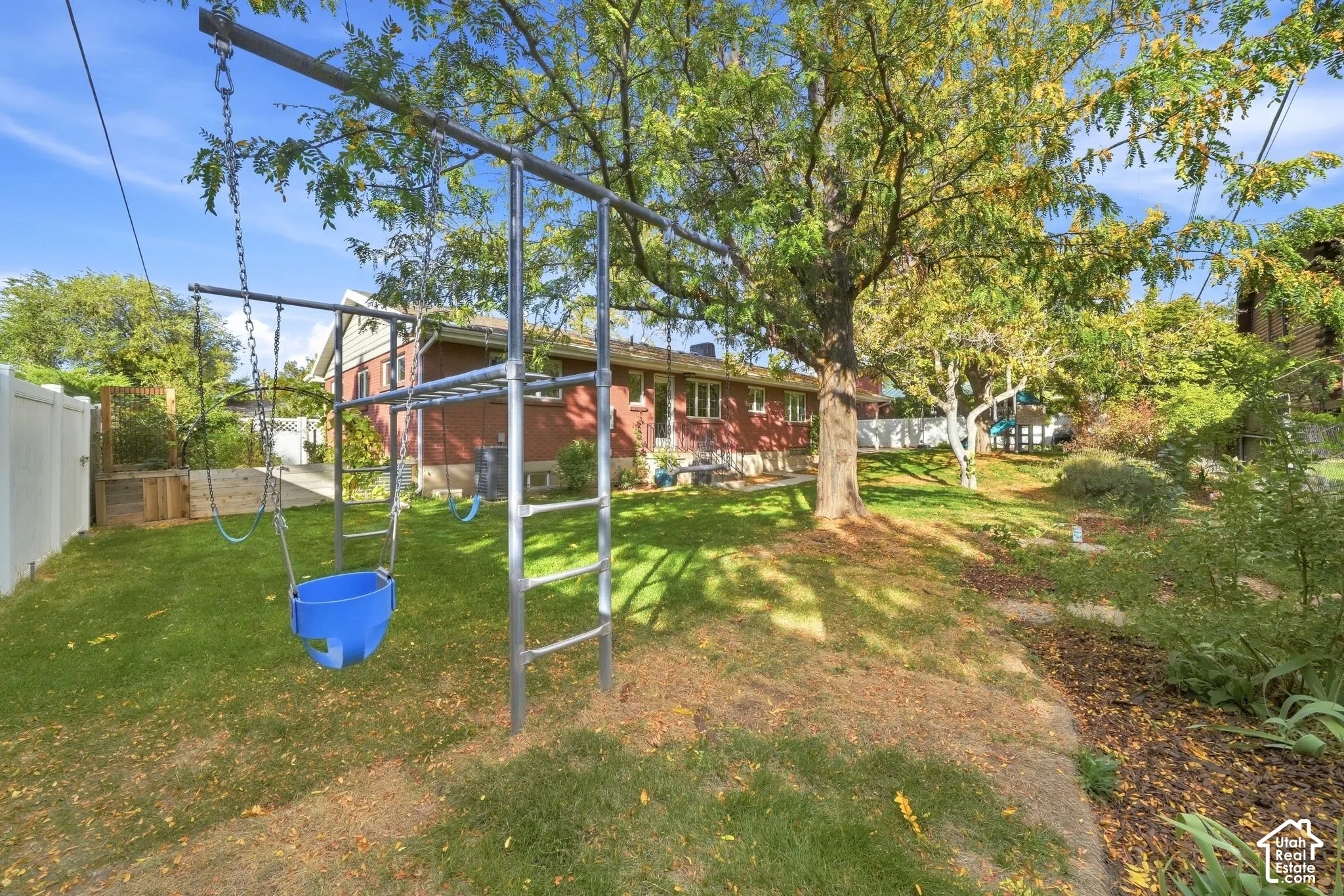 Secluded backyard with mature trees and a play structure behind the brick rambler.